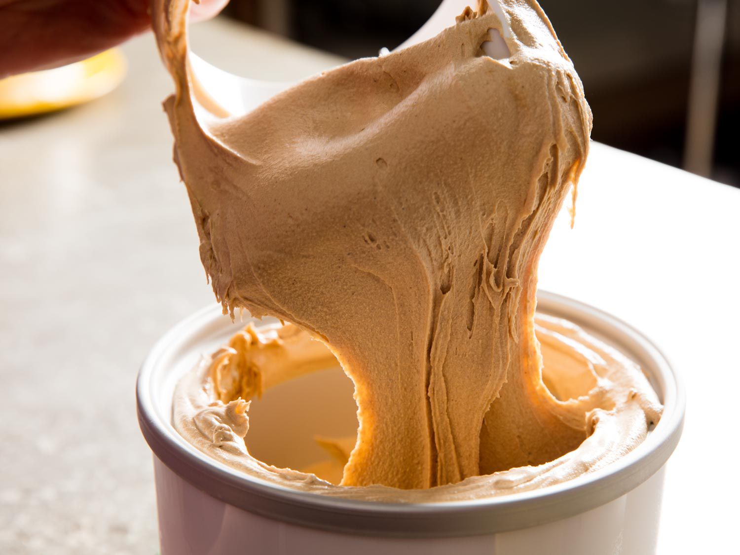 The dasher is removed from the ice cream maker's canister, trailing churned speculoos ice cream.