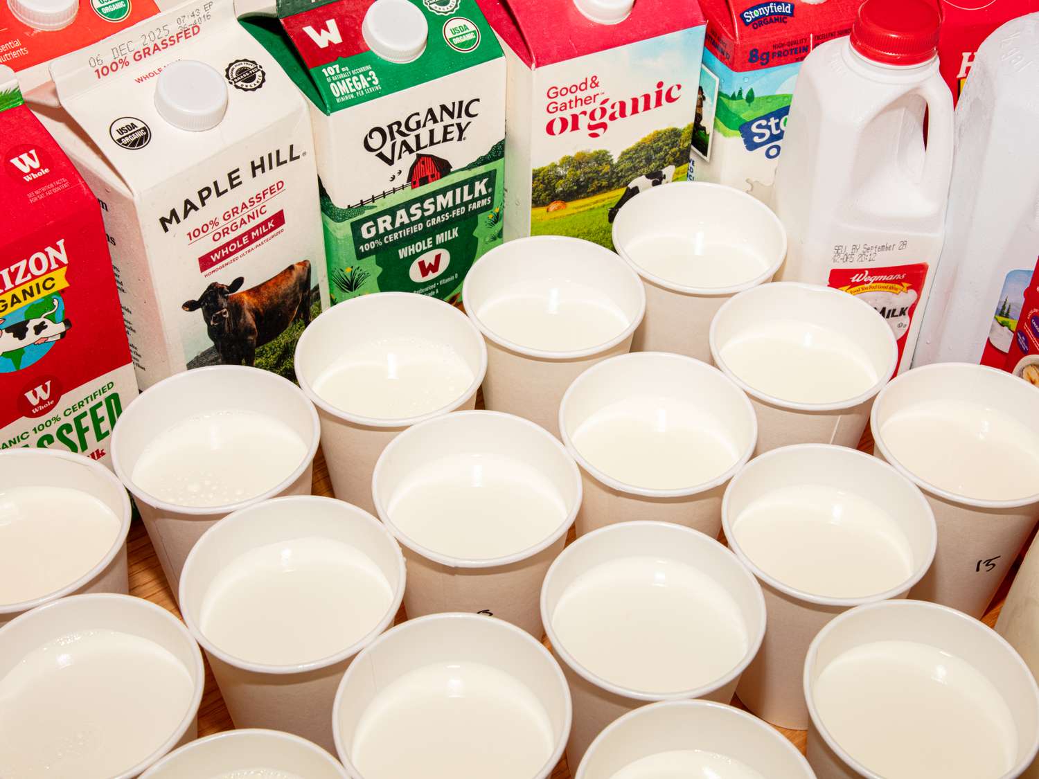 Various cartons and bottles of milk displayed behind rows of cups filled with milk