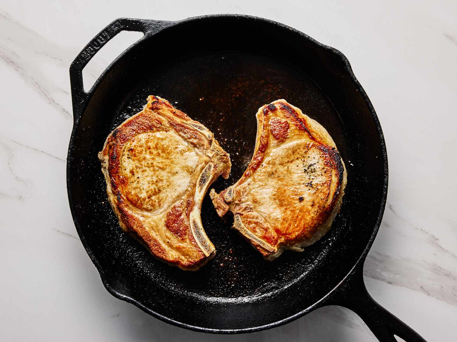 Two pork chops cooking in a cast iron skillet