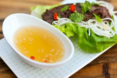A dish of nuoc cham on a plate containing lettuce, vermicelli and a piece of grilled meat.