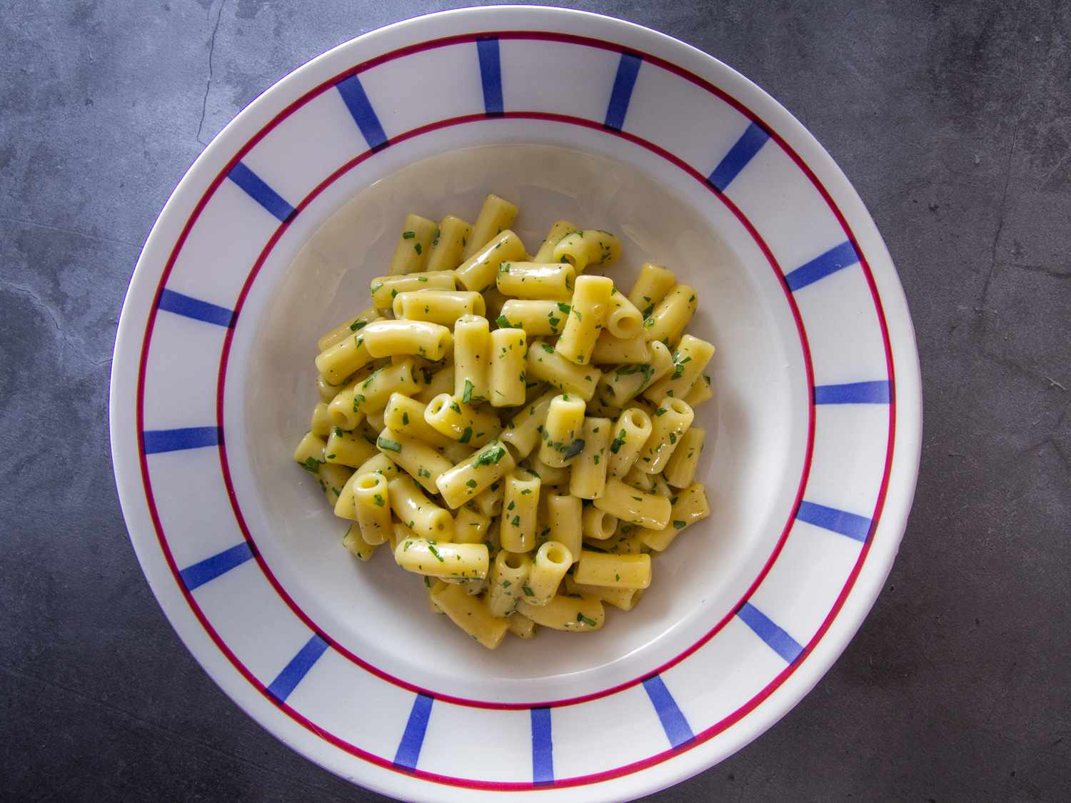 Finished pasta cacio e uova (Neapolitan pasta with eggs and cheese) in a white shallow bowl with a blue and red rim.
