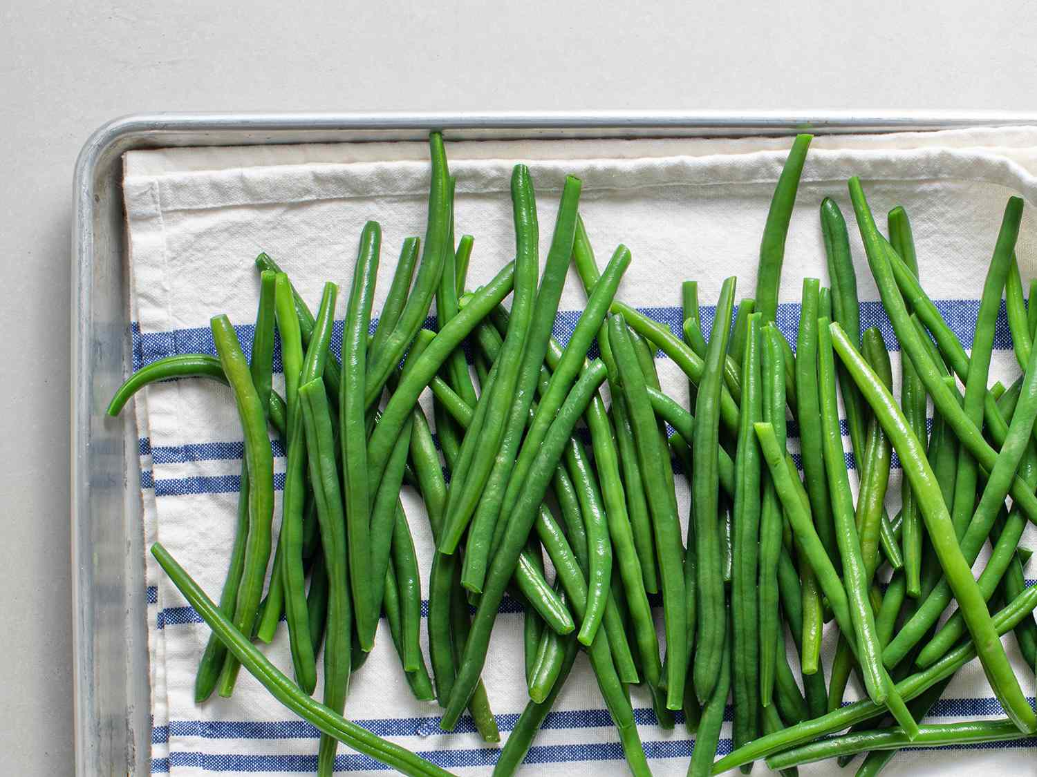 Blanched and chilled green beans drying on a dish towel in a baking sheet.