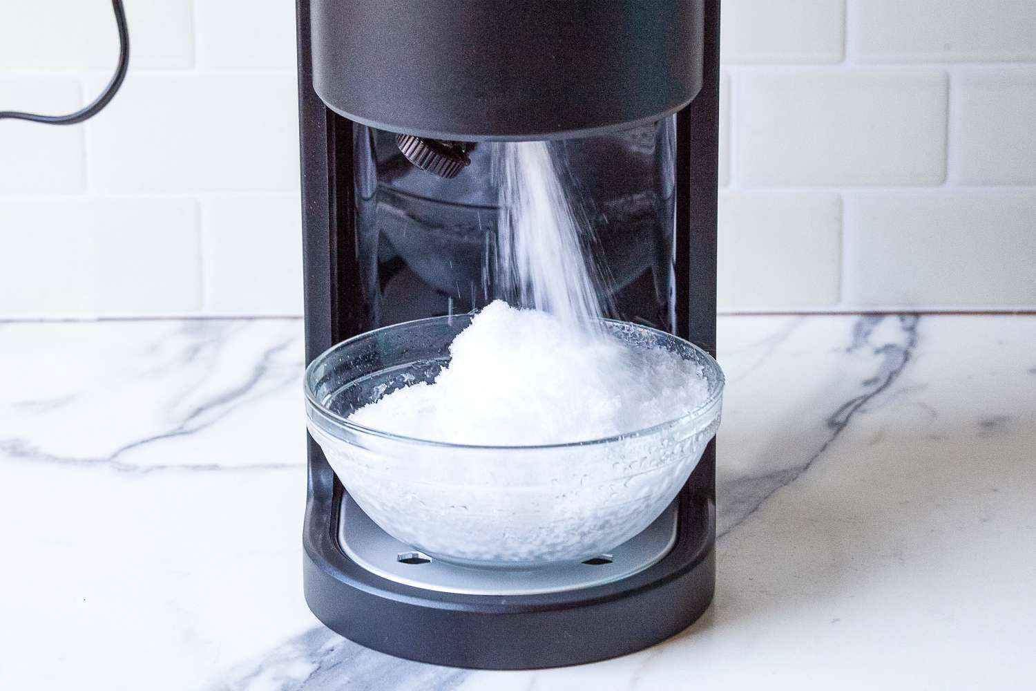 Hawaiian Shaved Ice HomePro Shave Ice and Snow Cone Machine (S777) dispensing crushed ice into a clear bowl on a counter