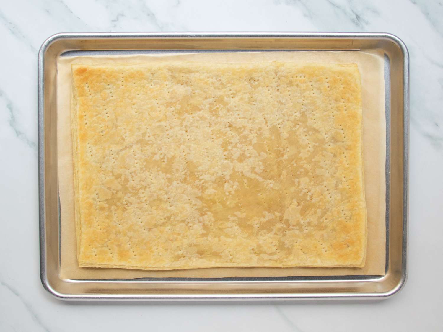 Par-baked, docked sheet of puff pastry in a rimed baking sheet