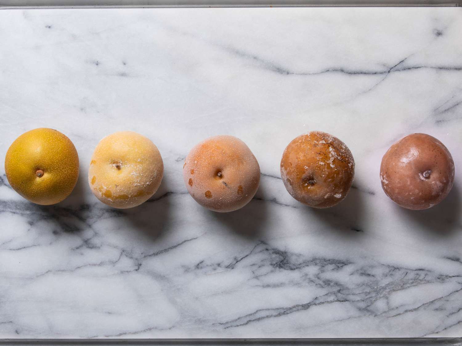 Frozen pears lined up at different stages in freezing and thawing process, with pears growing darker from left to right