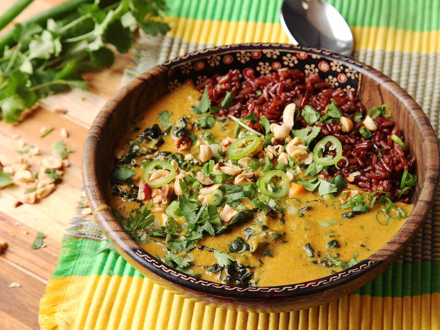 Bowl of peanut soup over red rice garnished with peanuts and herbs.