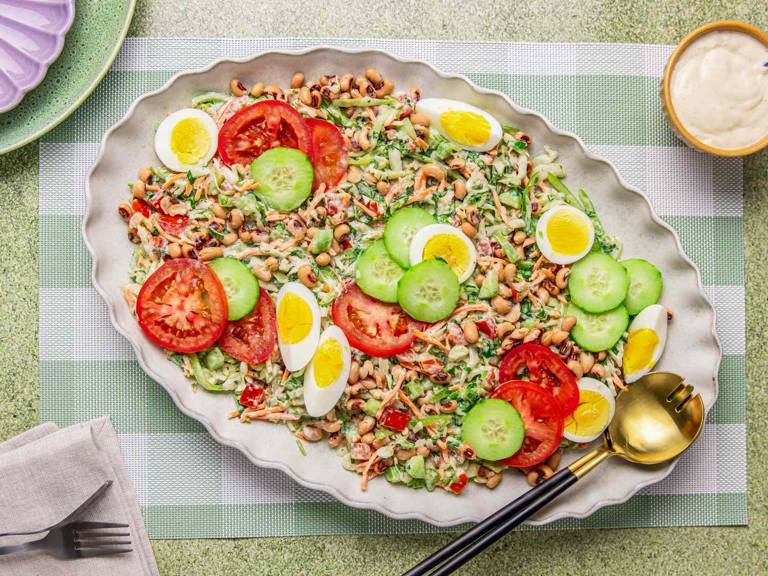 A platter of Nigerian salad topped with sliced eggs cucumbers and tomatoes displayed on a table with cutlery