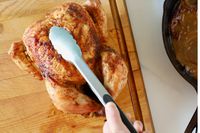 Hand picking up a whole chicken using the OXO Good Grips 12-Inch Tongs