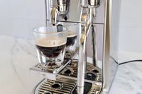 Espresso pouring from a coffee machine into a glass cup stainless steel design