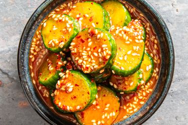 A bowl of marinated cucumber slices topped with sesame seeds and red chili flakes