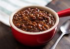 Red single-serving crock with slow-cooked baked beans.