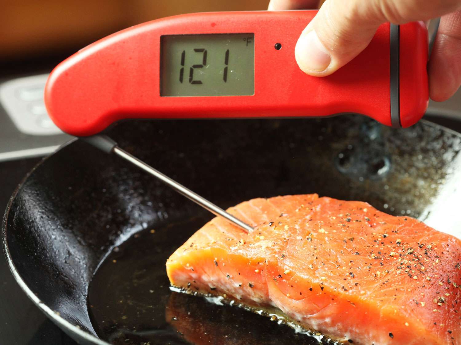Using an instant read thermometer to see that interior of searing salmon fillet is 121F.
