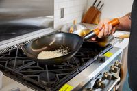 Hand holding the Yosukata Carbon Steel Wok Pan over a gas stove 