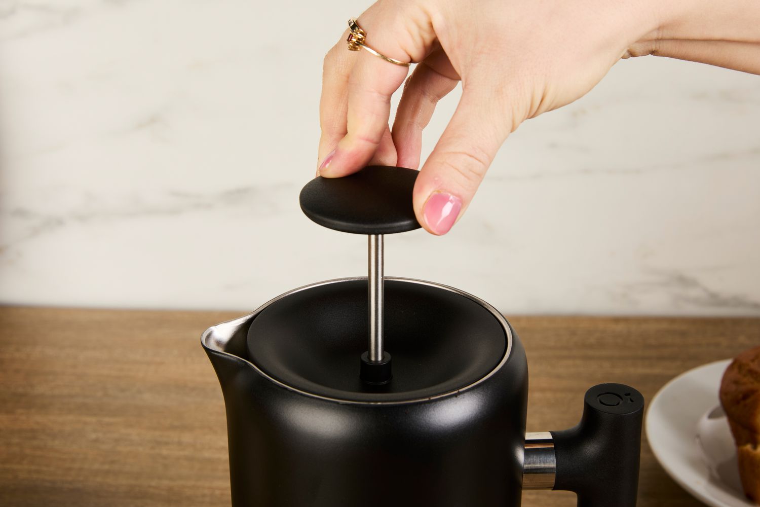 A person pressing down the plunger on the Fellow gooseneck kettle's lid.