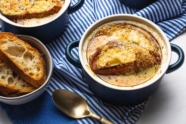 Overhead view of two bowls of french onion soup in small bowls on a striped blue background.