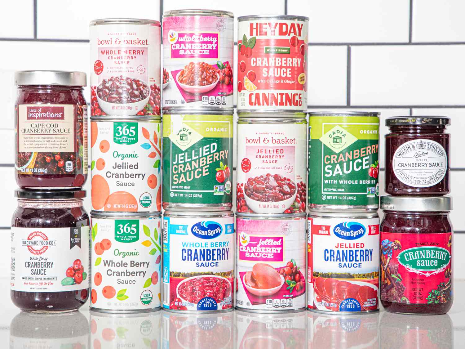 An assortment of canned and jarred cranberry sauces displayed on a counter in a tiled background setting