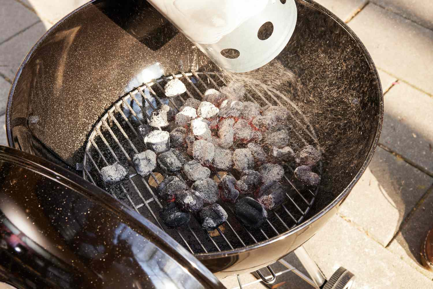 Coals being added to a charcoal grill.