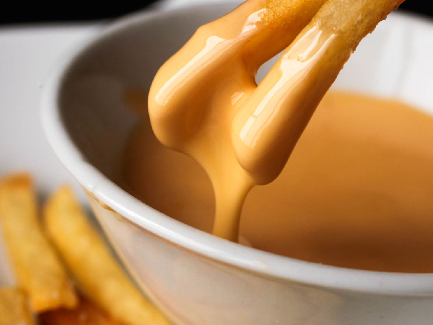 Fries being dipped into a cheese sauce.