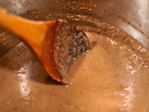 Cooking down pork liver sauce in a pot and stirring with a wooden spoon. 