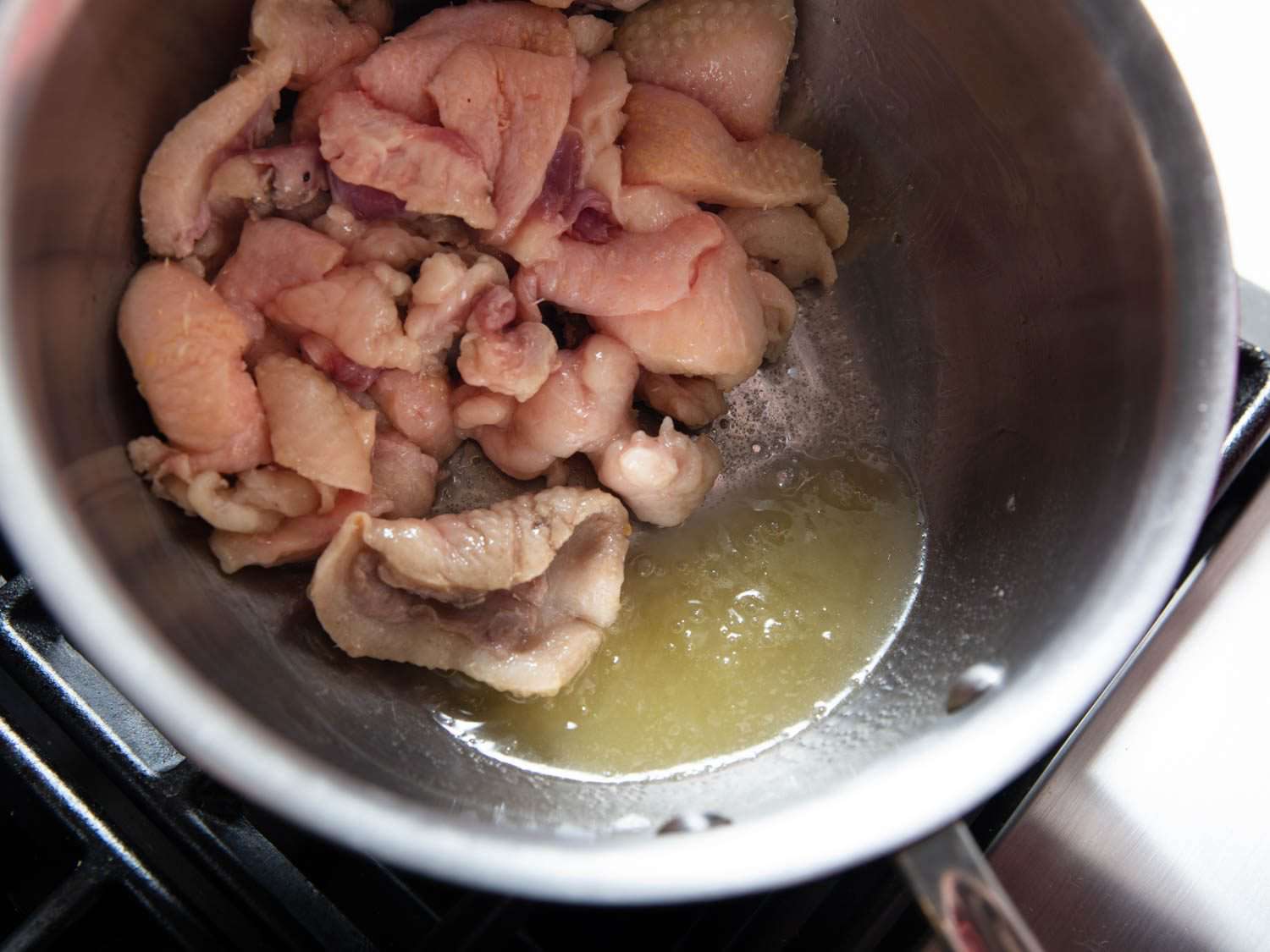 The pan of duck skin, water, and rendered fat is tilted so that the fat and water is pooled in the pan.