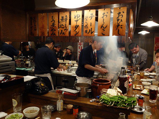 A view of cooks behind a full counter of customers at Saiseisakaba 