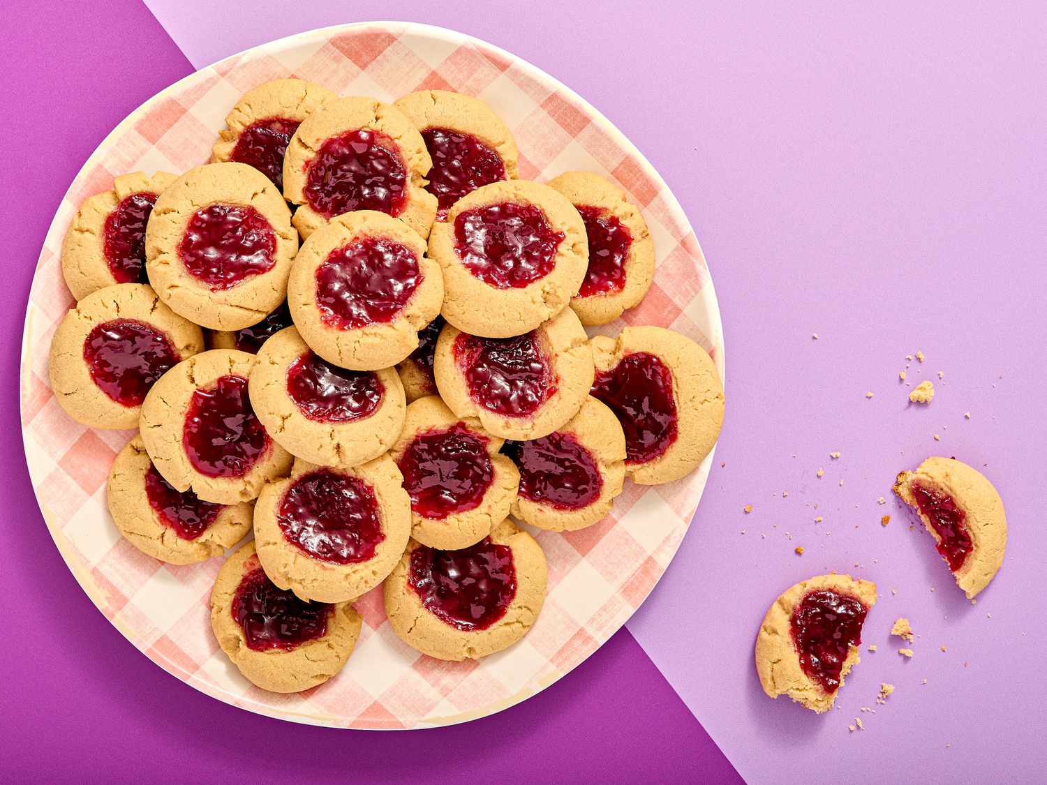 Plate of thumbprint cookies filled with jam, on a pink and purple background
