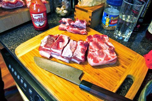 Cuts of pork belly resting on a cutting board with a chef's knife off to the side.