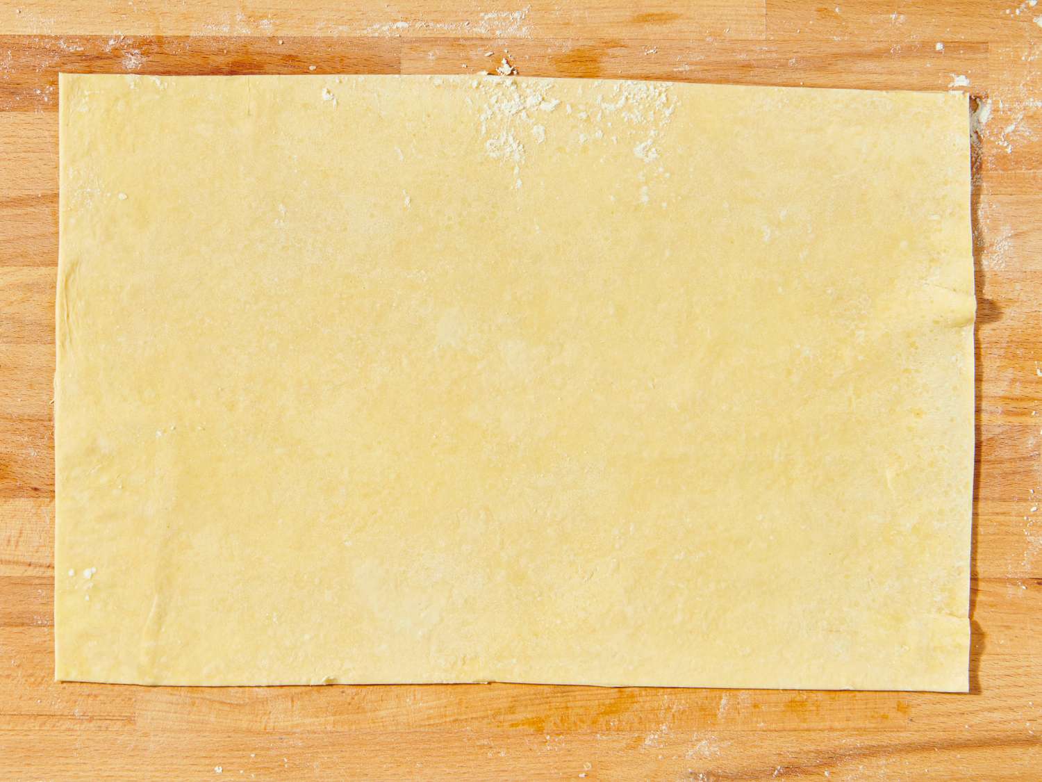 A sheet of pastry dough placed flat on a wooden surface