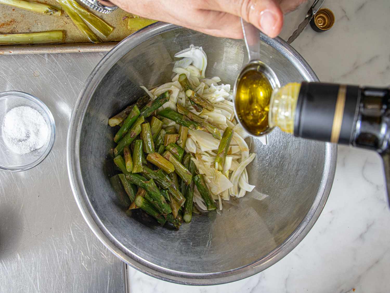 A bowl with vegetables being prepared, olive oil being poured from a spoon