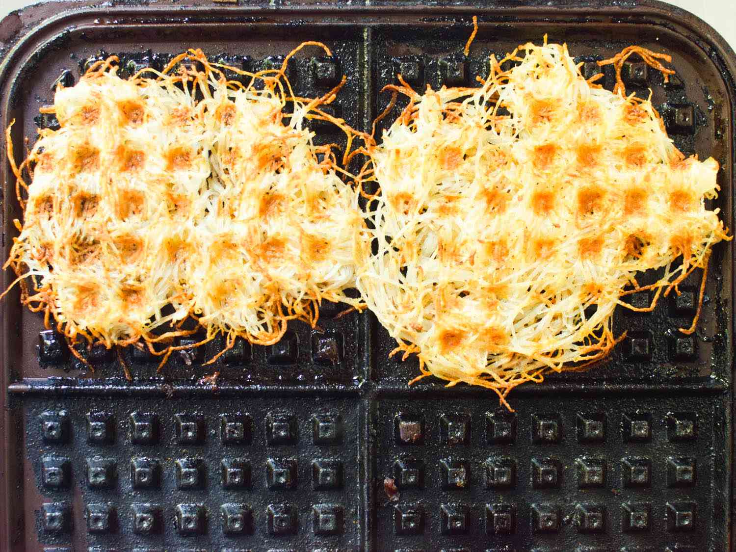 Finely shredded potatoes cooking in a waffle iron.