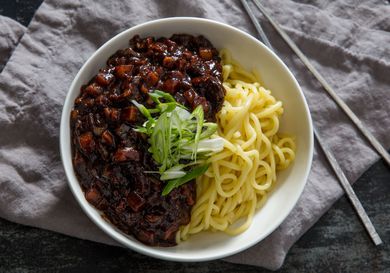 A bowl of jjajangmyeon with a thick and hearty black bean sauce on one side and fresh noodles on the other.