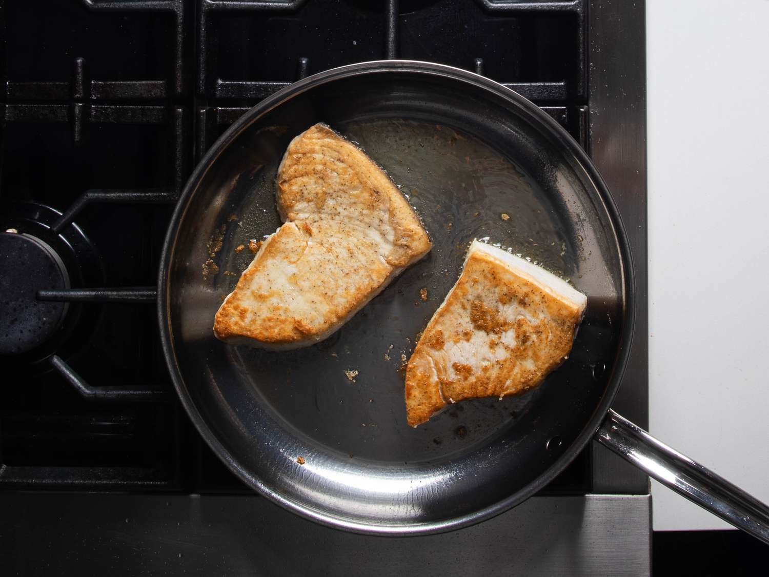 Browned swordfish steaks in the skillet right after being flipped.