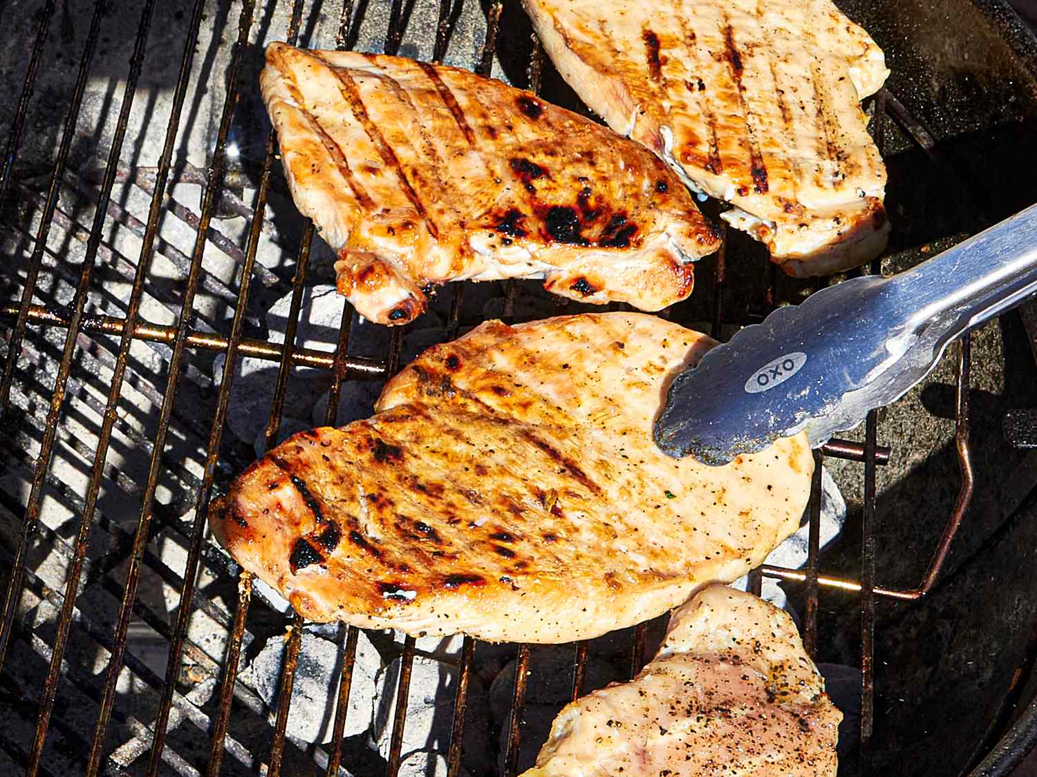Chicken breasts cooking on a grill with tongs holding one piece