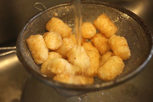 Rinsing strainer full of tater tots under running water.