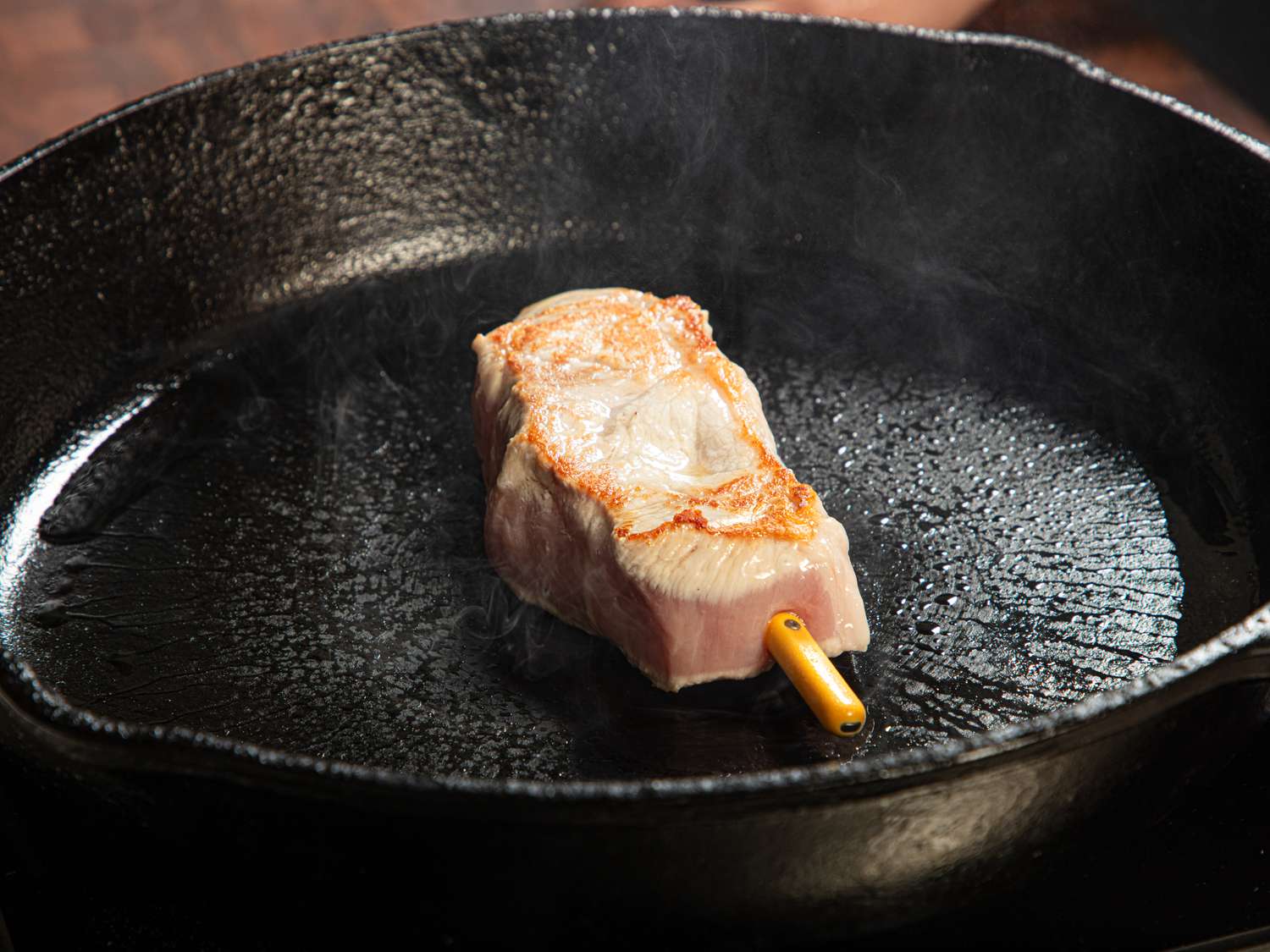 Cooked meat resting in a cast iron skillet with a thermometer inserted
