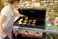 A person cooks hamburgers on the Weber Slate 28 inch Rust-Resistant 3 Burner Outdoor Griddle