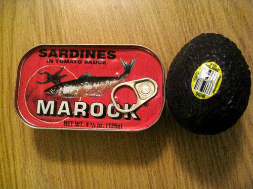 Can of oil-packed sardines next to a whole avocado.
