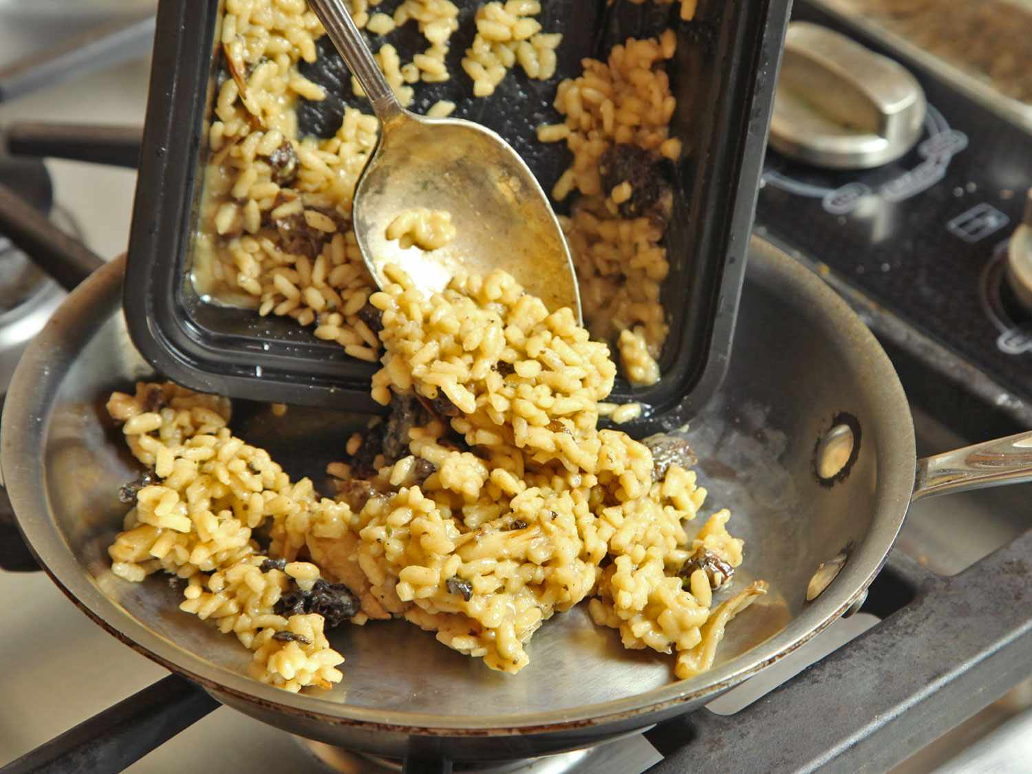 Par-cooked risotto is scraped from a storage container into a skillet.