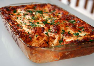 A rectangular glass baking pan of lasagna bolognese sprinkled with fresh chopped herbs.