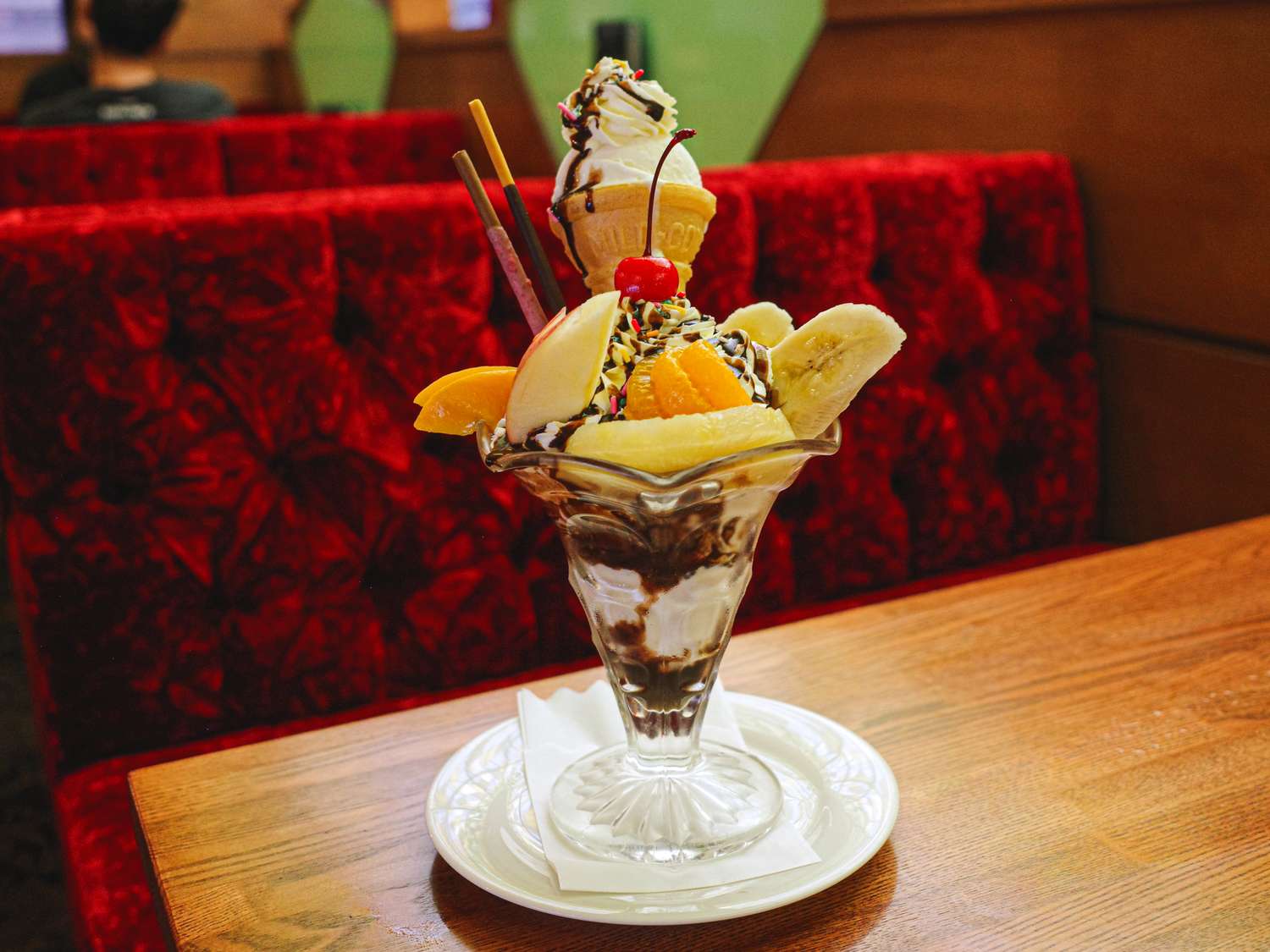 A dessert parfait served in a glass dish with fruit and toppings on a wooden table