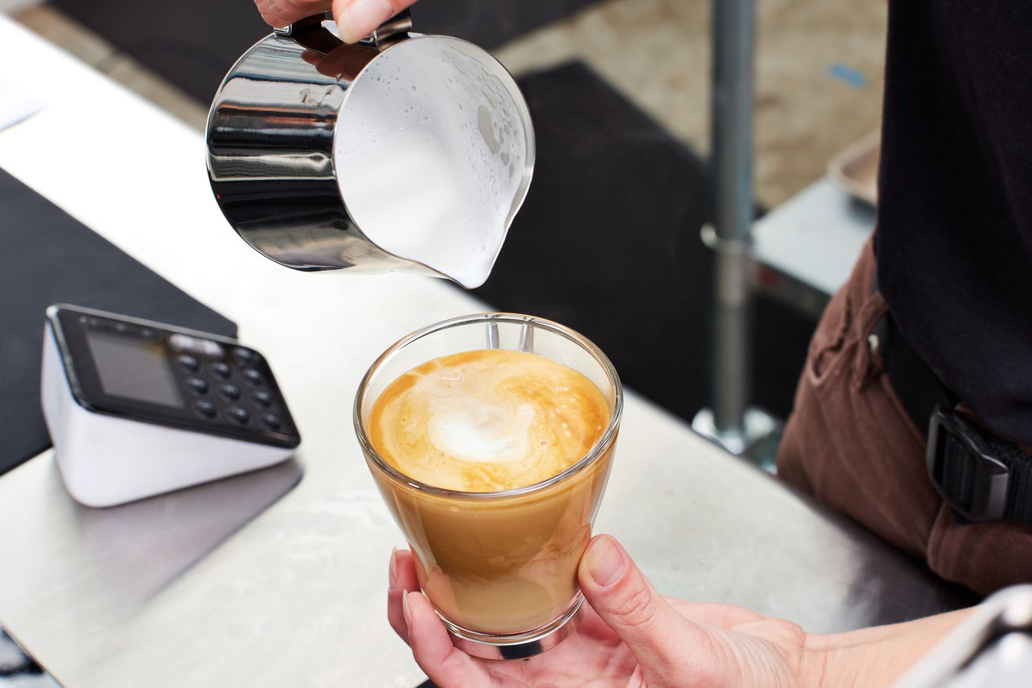 Closeup of a person pouring milk into a brewed cup of espresso
