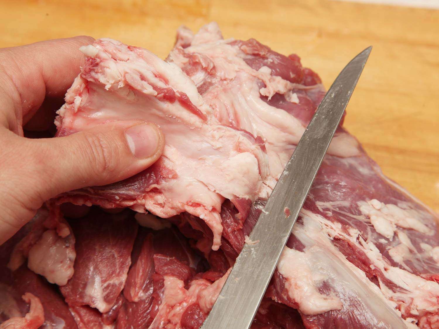 Author trimming large pockets of fat from the interior of a butterflied leg of lamb.