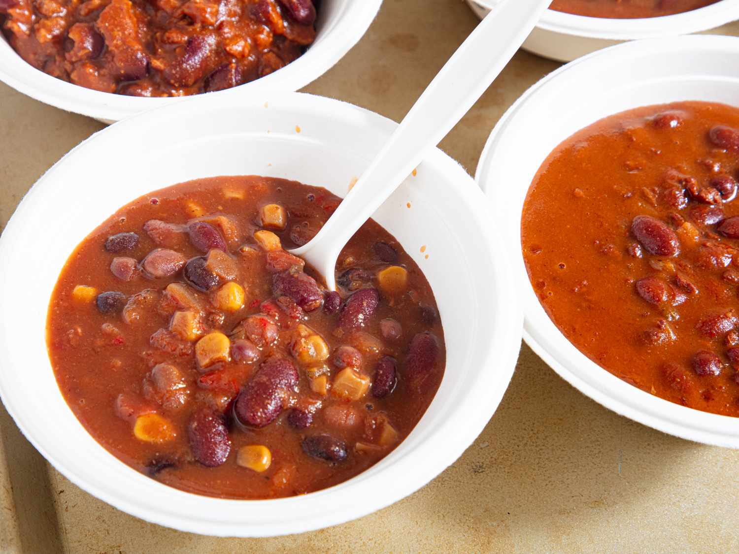 Bowls of chili with beans and corn served with a spoon