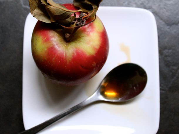 Overhead shot of an apple and a spoon filled with boiled cider syrup.