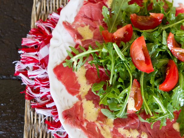 A plate of beef carpaccio topped with arugula and tomato wedges.