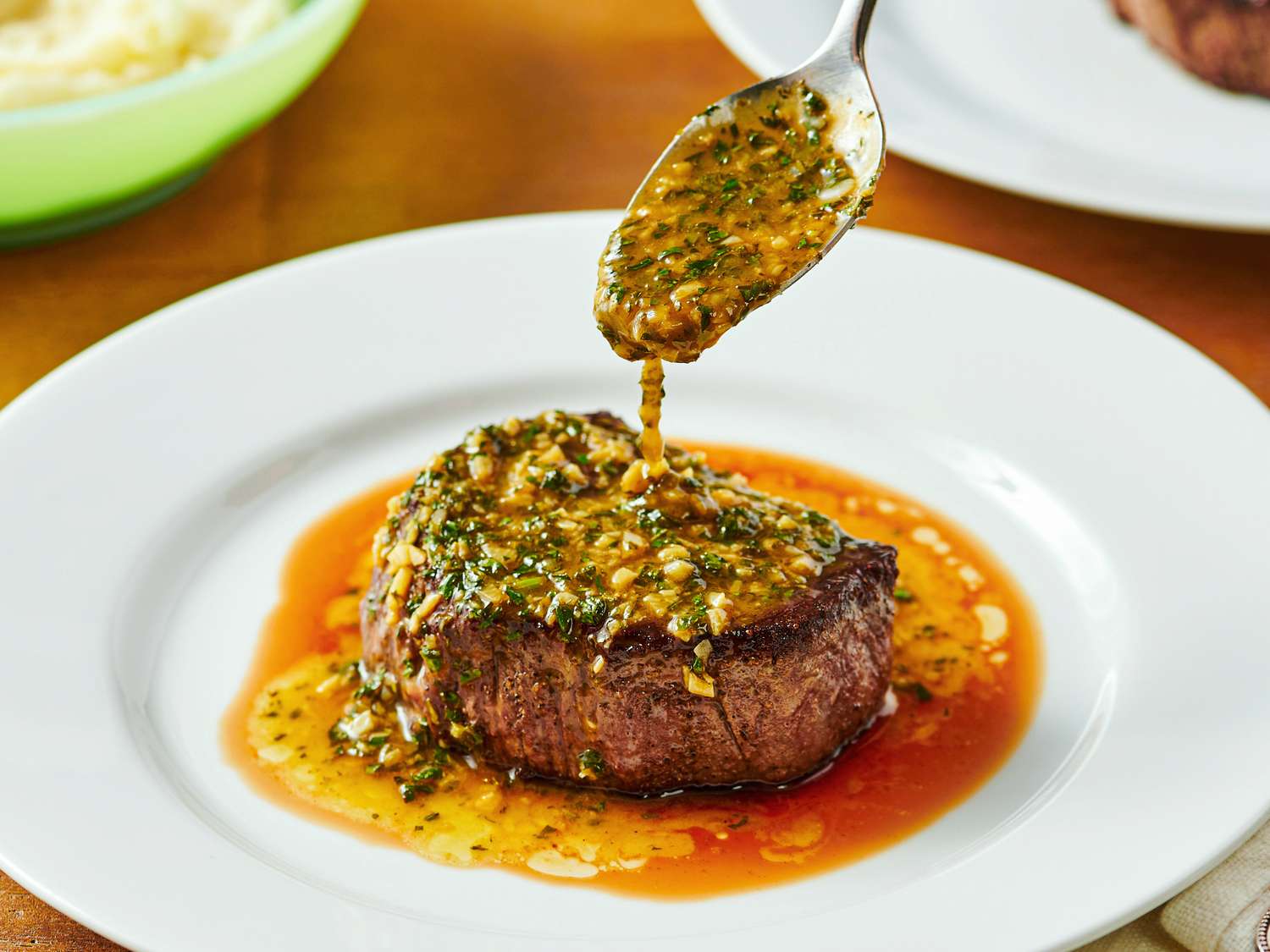A plate of steak served with a sauce being spooned onto it