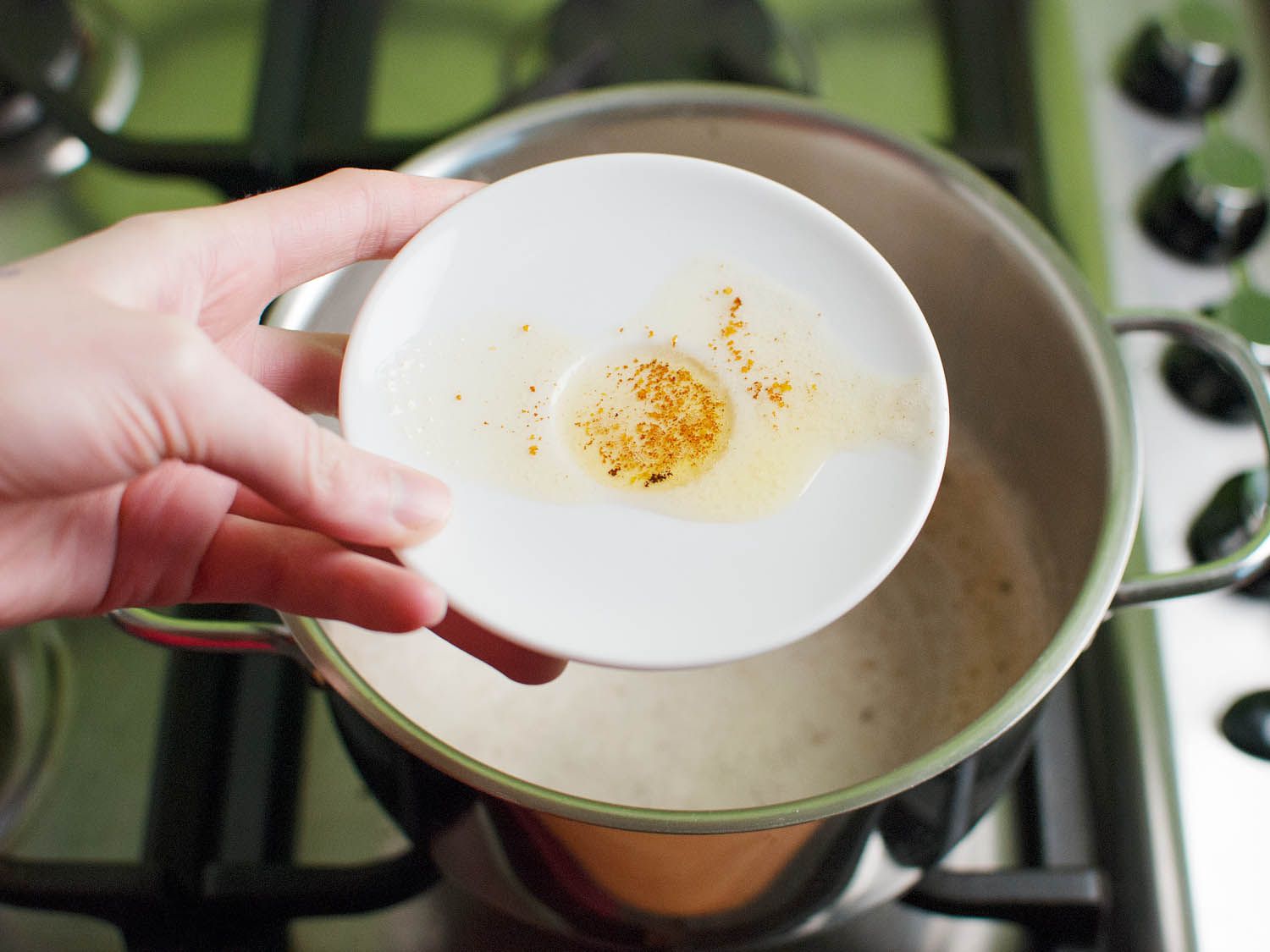 Some browned butter spooned into a saucer. The browned milk solids are visible against the white saucer. The saucer is held by a hand.