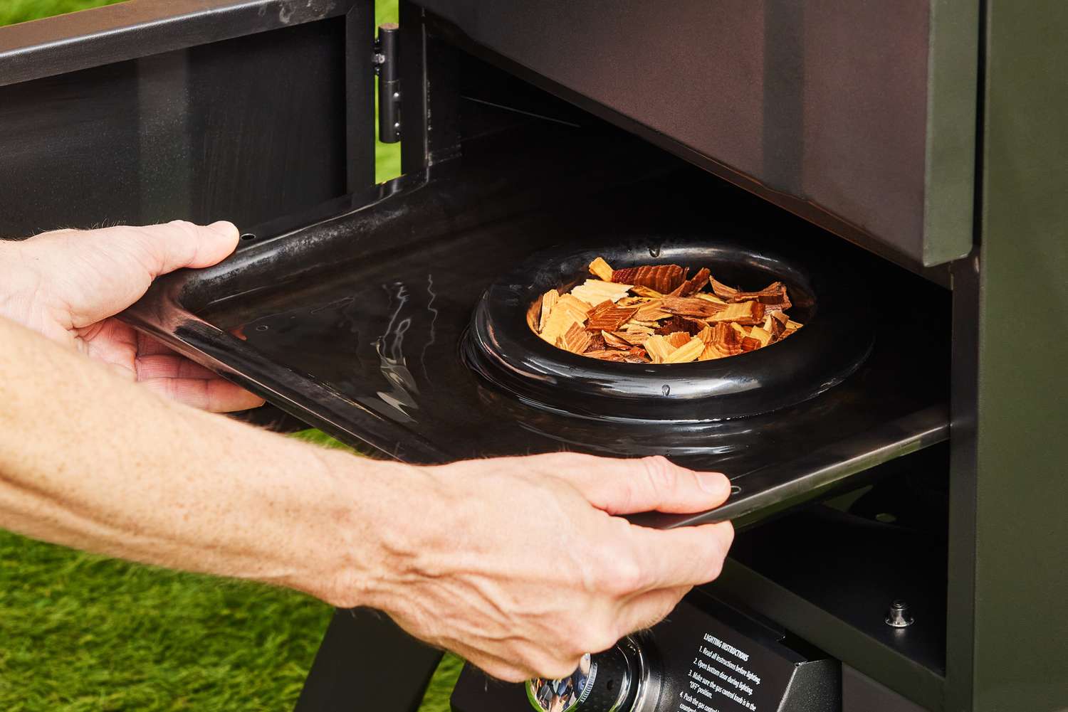 A person adding wood chips to the fuel chamber of the Cuisinart Vertical Propane Smoker