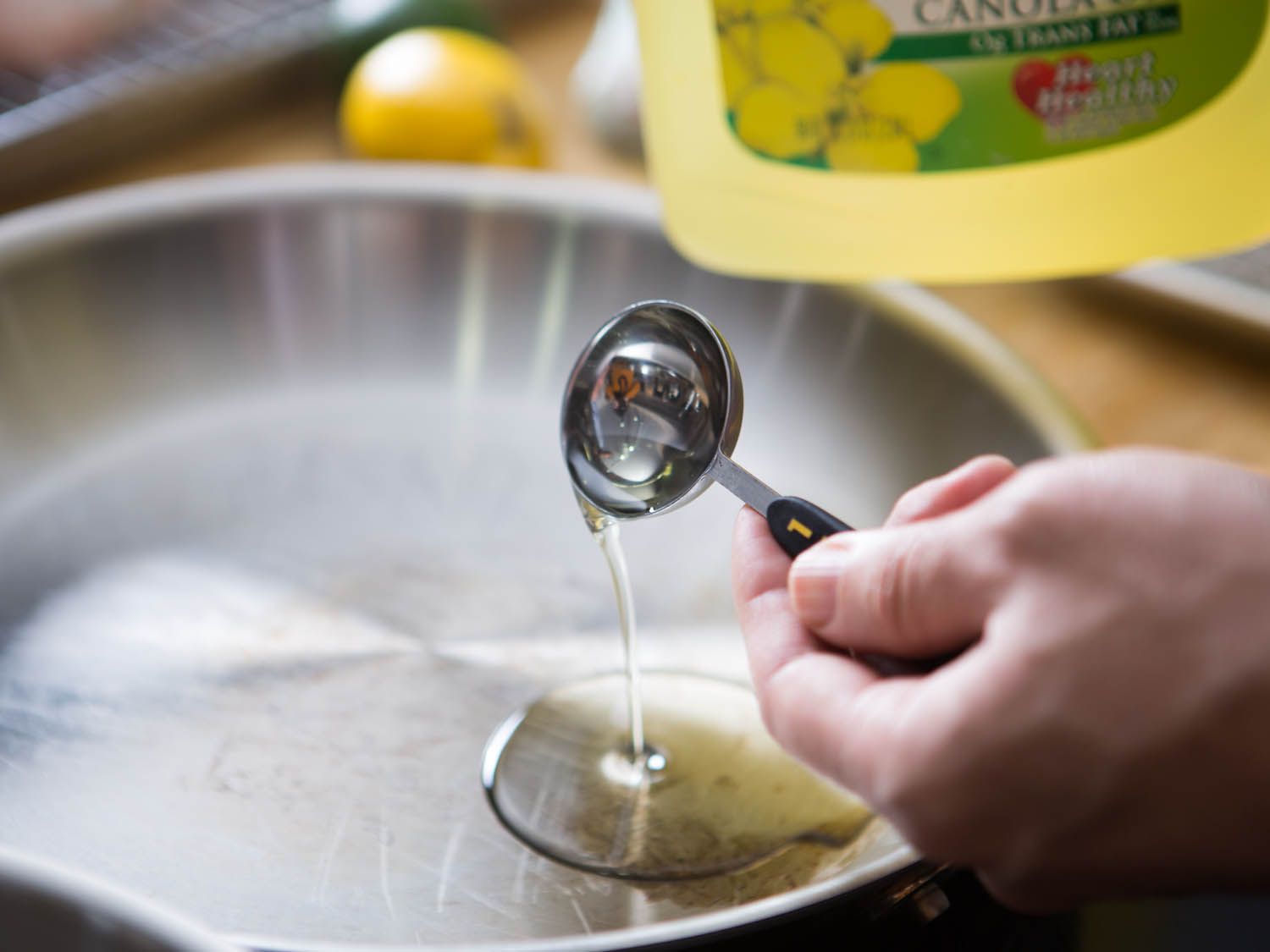 Pouring a tablespoon of canola oil into a stainless steel pan.