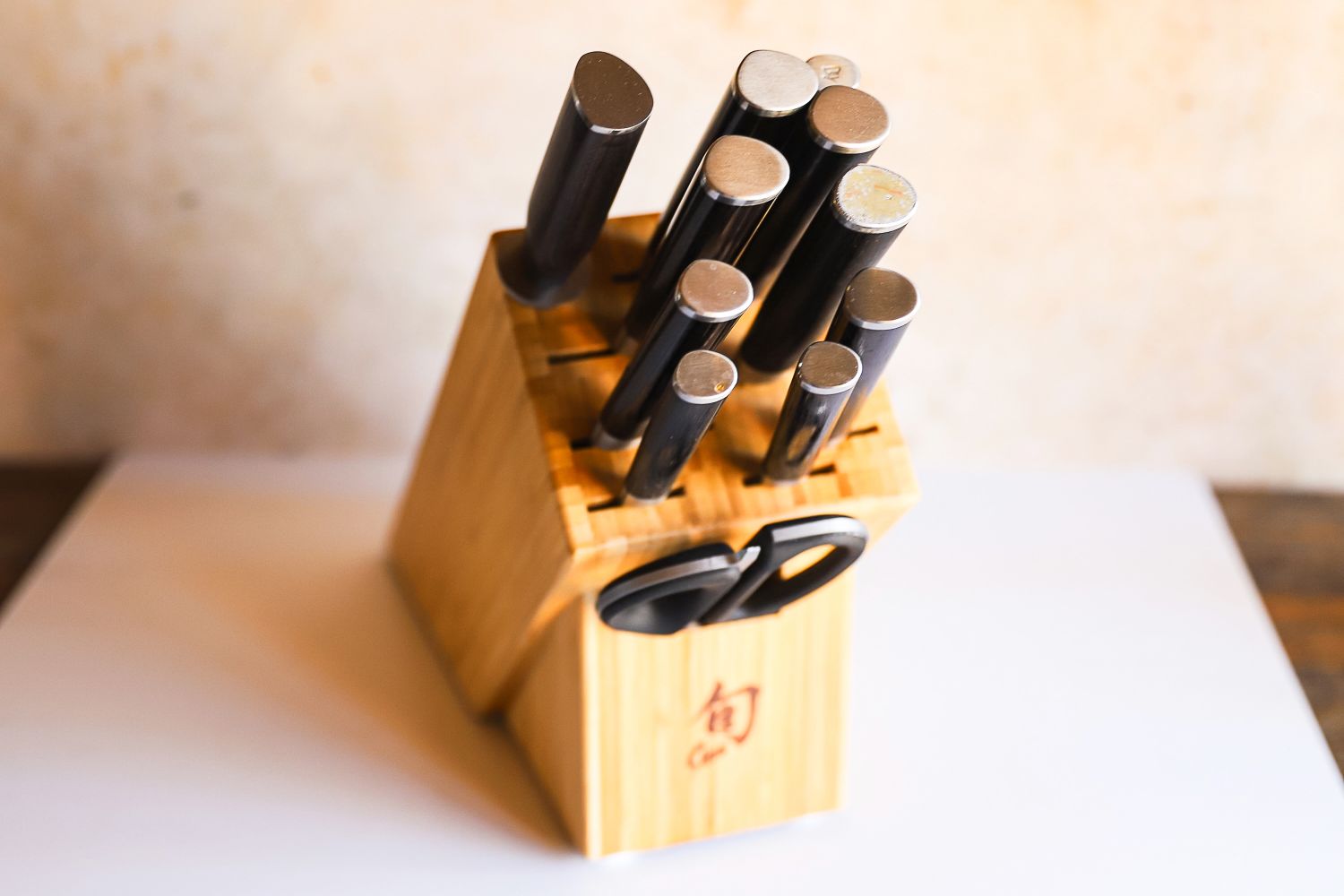 A set of Shun kitchen knives in a wooden knife block including scissors arranged neatly on a counter